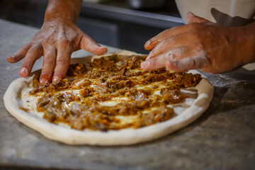 Pizzaiolo mentre stende il sugo di Genovese su una pizza napoletana sul banco da lavoro