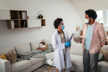 Doctor having consultation with man whose son is sick and lying on bed near them