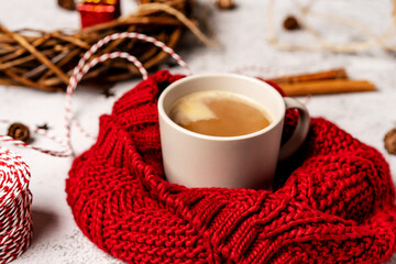 Coffee mug in a soft red winter scarf on a gray background with Christmas decorations. Christmas coffee break for home recreation. The view from the top