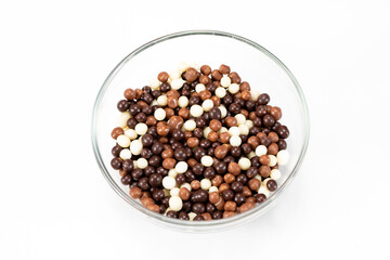 Mix of crispy chocolate balls in glass bowl for decorating cakes, pastries, handmade chocolates, cupcakes and desserts. Filling for yogurt, dressing. Vegetarian food concept. Isolated white background