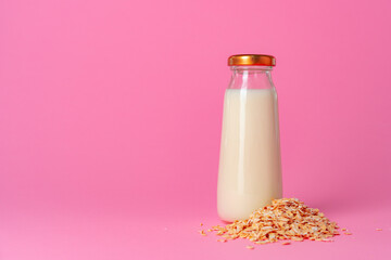 Oat milk in glassware and dry oat flakes on pink background