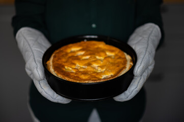 woman holding a fresh apple pie with grey pot gloves