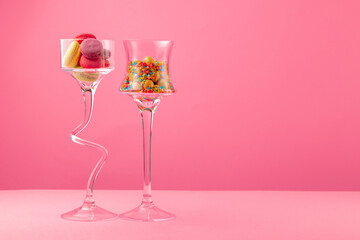 Glass containers with candies against pink background