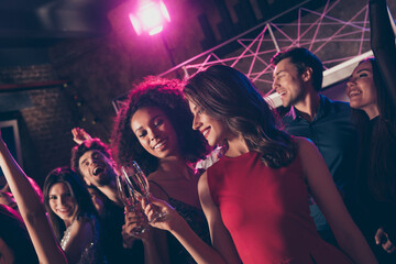 Photo portrait of two girls clinking champagne glasses with other people at big party in background