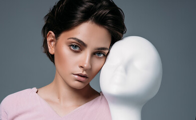 Portrait of young brunette woman with mannequin face isolated on gray background