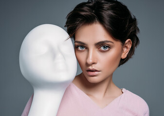 Portrait of young brunette woman with white mannequin face isolated on gray background