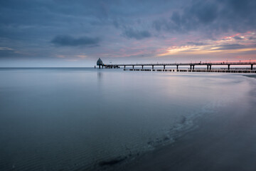 Fototapeta premium Cloudy sunrise at the beach at baltic sea with pier, Zingst, Western-Pomerania, Germany