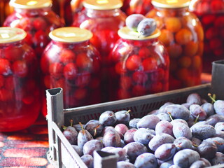 Preservation for the winter is in the pantry or cellar. A box with a blue plum on a background of finished compote in large glass jars.