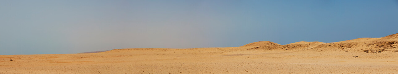 Super wide panorama of a desert landscape with a hazy blue sky.