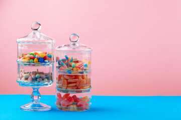 Glass containers with candies against pink background