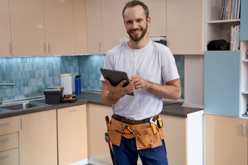 Young caucasian house master with tablet standing in kitchen