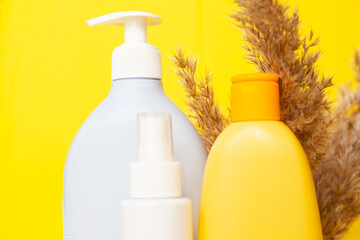 cosmetic bottles on yellow background, fluffy soft twigs