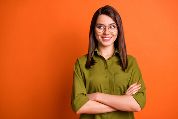 Photo portrait of curious girl smiling with crossed hands looking at empty space isolated on bright orange color background