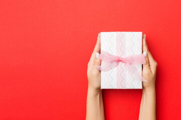 Female's hands holding striped gift box with colored ribbon on red background. Christmas concept or other holiday handmade present box, concept top view with copy space