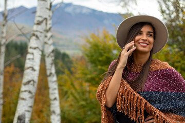 A smiling pretty woman with a hat is having a phone call in the nature