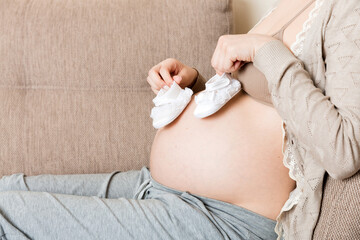 Small shoes for the unborn baby in the belly of pregnant woman ion sofa at the house