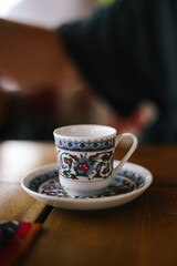 Patterned coffee cup on a saucer stands on a table in a restaurant. Red-blue drawings of flowers and lines. Beautiful composition and background. Crimean cuisine