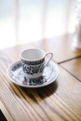 Empty patterned coffee cup on a saucer stands on a table in a restaurant. Red-blue drawings of flowers and lines. Shadows and light, beautiful composition. Crimean cuisine