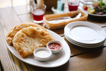 Three fresh hot fragrant delicious chebureks lie on a white plate with sour cream, ketchup sauces. Crimean cuisine lunch  in the restaurant. Closeup, food background. 