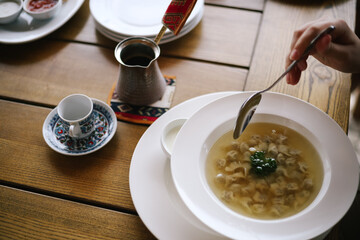 Soup with dumplings. Hand holding spoon. Lunch at the restaurant. Crimean cuisine. Turk for coffee and empty pot and white plates.