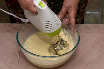 Women's hands knead the dough with different ingredients-milk, flour, butter, sugar and egg for homemade pancakes.