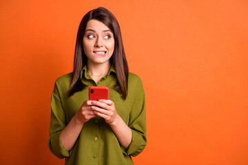 Photo of guilty young girl hold smartphone bite lip look side empty space wear green shirt isolated...