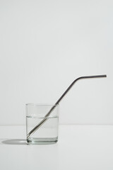 Transparent glass of water on white with sustainable metal straw