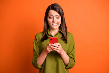 Photo of scared young girl hold telephone bite lip look screen wear green shirt isolated orange color background