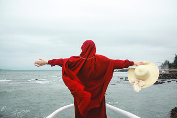 joyful woman with red scarf standing on the front of the boat deck looking at the sea and raising her hands, vacations and freedom lifestyle concept