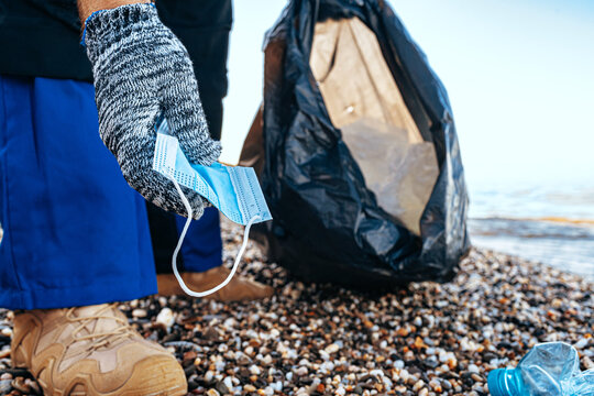 Man volunteer collecting used medical masks on the beach near the ocean