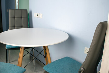 Modern kitchen or living room interior. Round white wood table with soft gray chairs near blue wall.