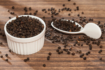Piper nigrum - black peppercorns; photo on dark wooden background.