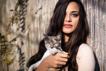 Beautiful young girl holding a calico cat. Outdoors photo - obrazy, fototapety, plakaty
