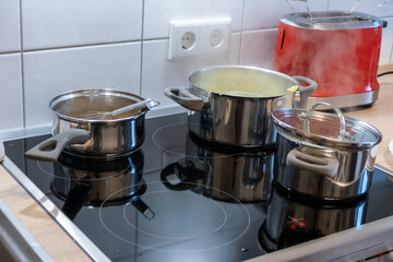 Cooking on cooker in the kitchen with hot steam and pots on a ceran stove to cook delicious meals for the family as healthy nutrition and a yummy lunch and dinner preparation