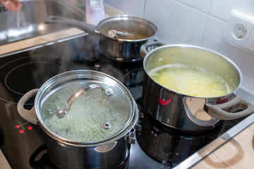 Cooking on cooker in the kitchen with hot steam and pots on a ceran stove to cook delicious meals for the family as healthy nutrition and a yummy lunch and dinner preparation