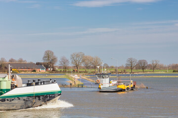 Obraz premium Ferry on the Dutch flooded river IJssel in the province of Gelderland with ship passing by