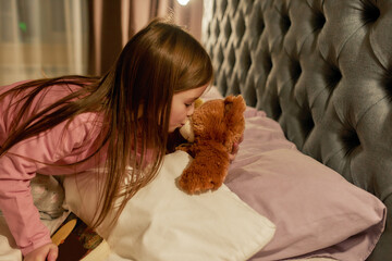 A cute small girl kissing a teddybear in his nose wishing goodnight before sleeping