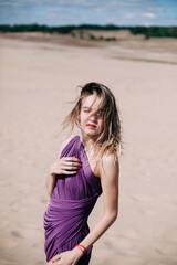 Fototapeta na wymiar Young, slender girl with purple cloth poses in the desert