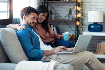 Happy beautiful couple using computer while sitting on the couch at home.