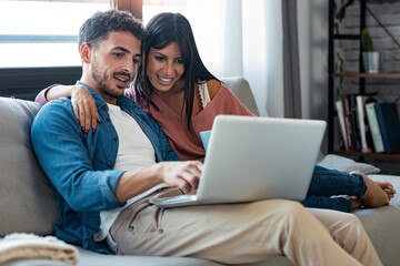 Happy beautiful couple using computer while sitting on the couch at home. - Powered by Adobe
