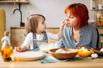 Cook together at home. Red-haired grandmother and little granddaughter cook pizza in a cozy home. Have fun in the kitchen