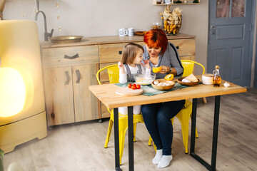 Cook together at home. Red-haired grandmother and little granddaughter cook pizza in a cozy home. Have fun in the kitchen
