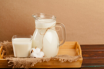 Pitcher of fresh milk on wooden table against beige background