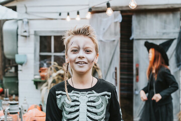 a boy in a skeleton costume with a painted face on the porch of a house decorated to celebrate a Halloween party