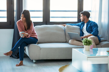 Angry young couple sitting on couch together and looking to opposite sides at home.