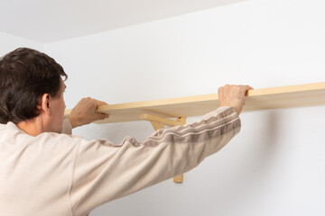A man hangs a shelf in an apartment on a white wall, a worker checks the evenness of the shelf