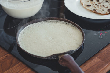 Baking pancakes in a frying pan close-up, ready-made pancakes on a plate.