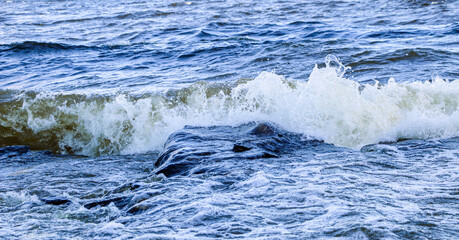 Naklejka premium waves run onto the shore and crash against the rocks, creating many splashes and splashes near the shore. river surf in stormy weather near a stone pebble coast with foamy splashing waves.