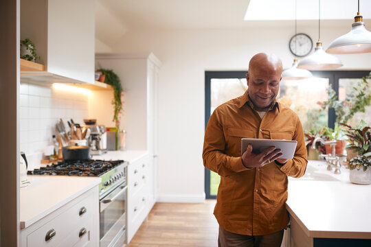 Mature Man At Home In Kitchen Looking At Digital Tablet
