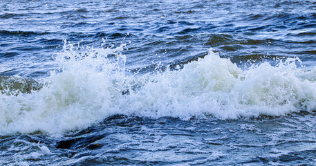waves run onto the shore and crash against the rocks, creating many splashes and splashes near the shore. river surf in stormy weather near a stone pebble coast with foamy splashing waves.